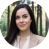 Smiling woman with long dark hair, wearing a blazer, in a forest setting