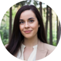 Smiling woman with long dark hair, wearing a blazer, in a forest setting